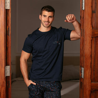 Man in navy t-shirt and patterned shorts standing in a doorway.